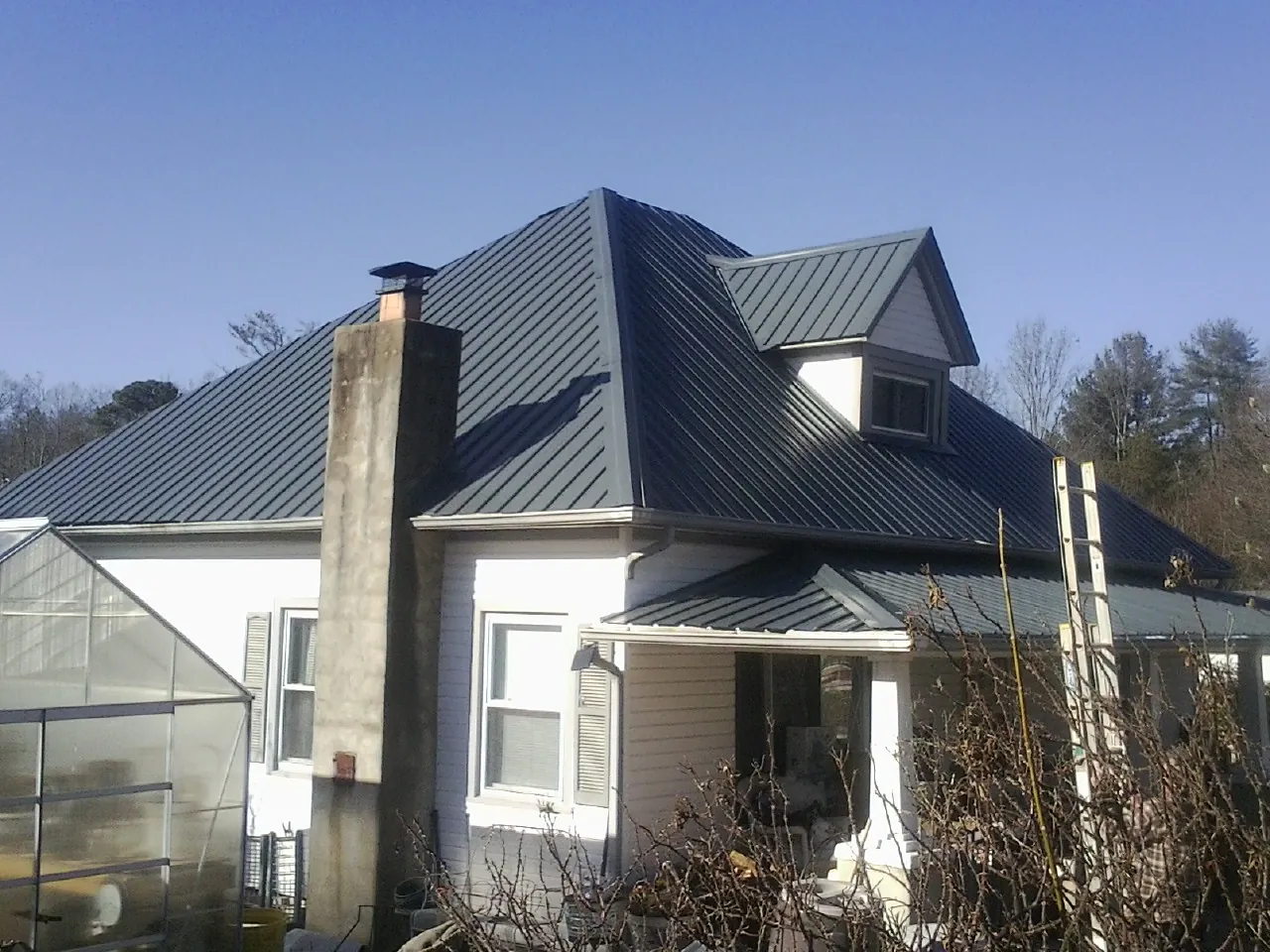 Dark blue standing seam metal roof on a white farmhouse with dormer — Slate & Tile Roof Repair by Roofing Brothers in Shutesbury