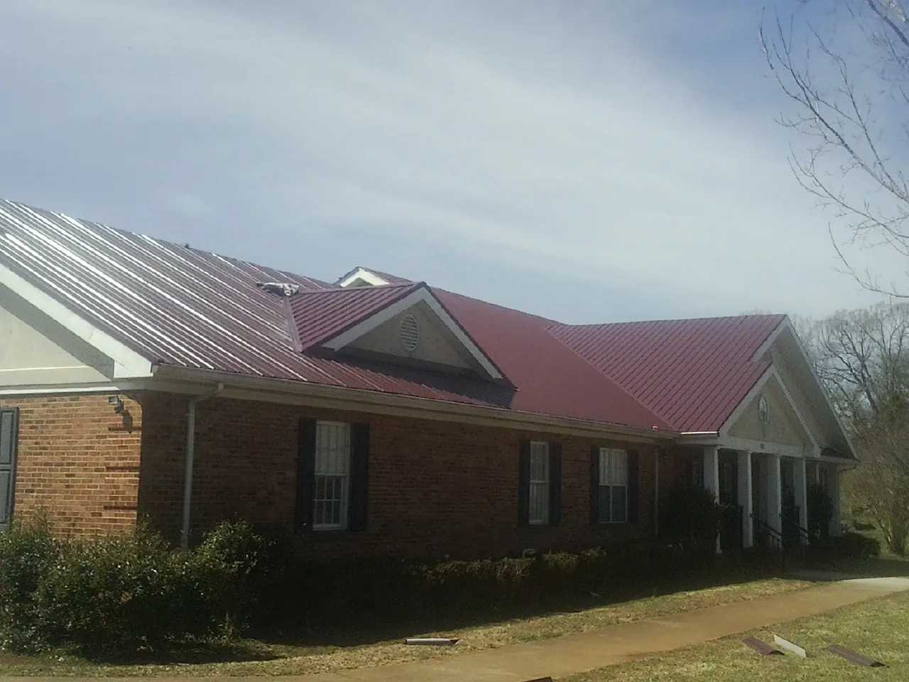 Red metal roof with gabled entries on a long brick building, from a Hail Damage Roof Repair job in Shutesbury