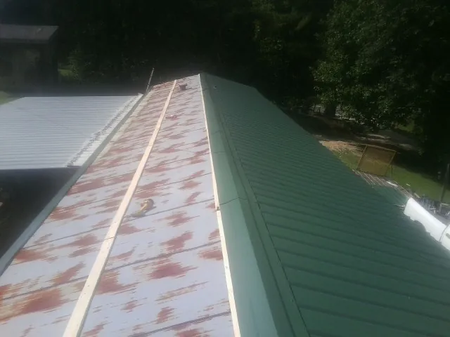 Old rusted panels beside newly installed green metal roofing — Wind Damage Roof Repair by Roofing Brothers in Shutesbury