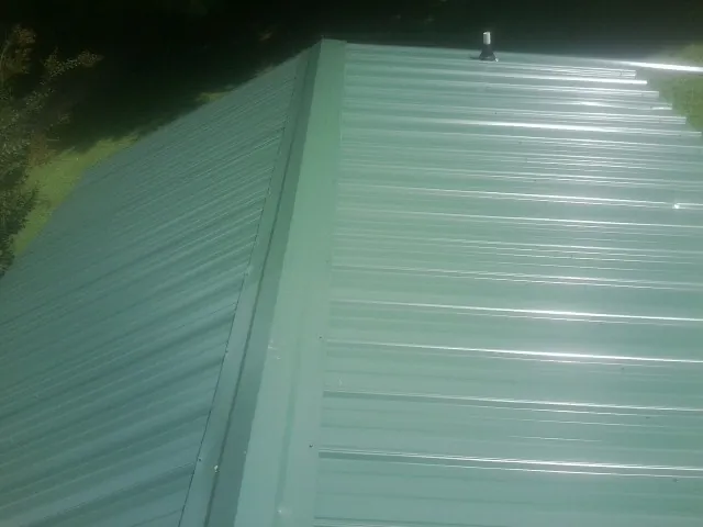 New green metal panels meeting at the ridge of a roof — Flat Roof Repair work by our crew in Shutesbury