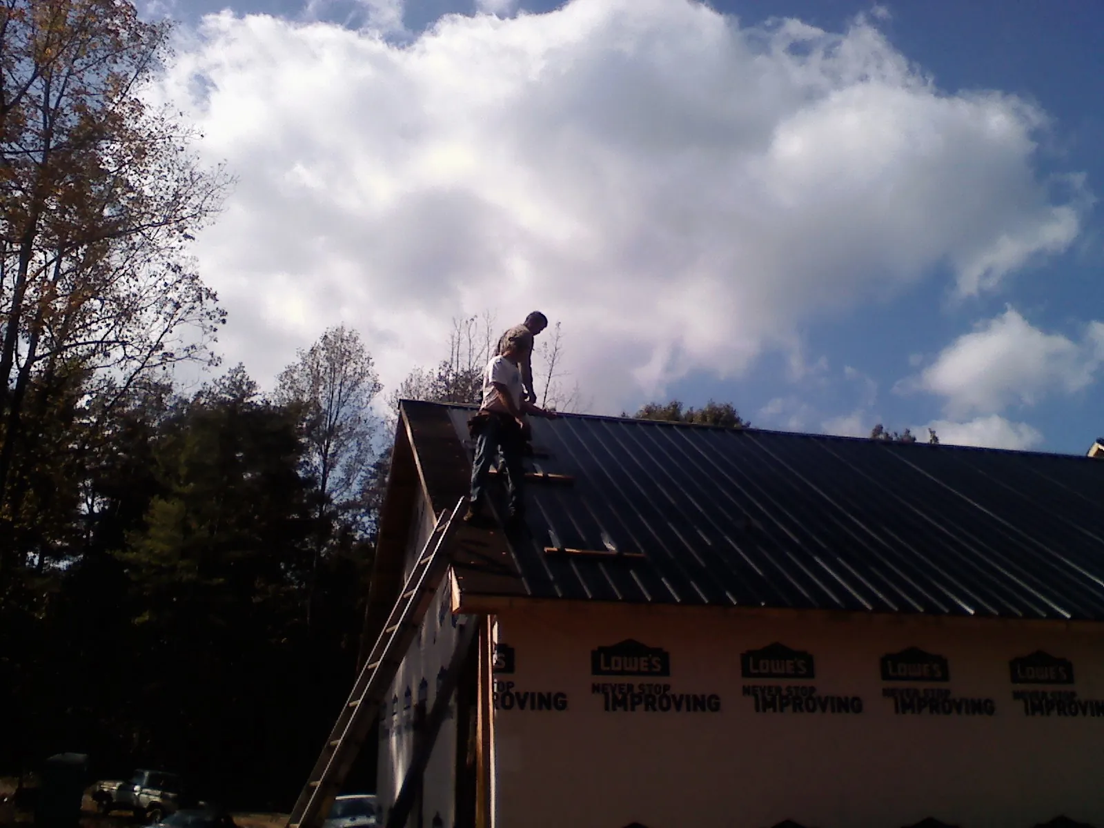 Roofer fastening dark metal panels high against a cloudy sky, from a Roof Inspection job in Shutesbury