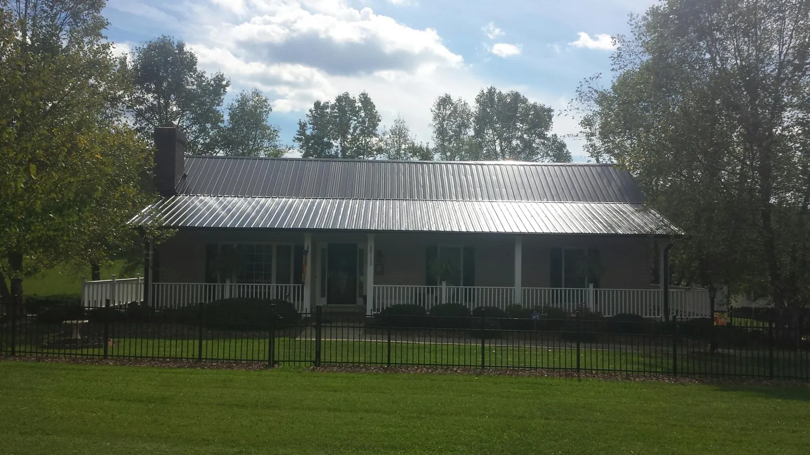 Gray metal roof on a brick ranch with a full width front porch — Gutter Guard Installation work by our crew in Shutesbury