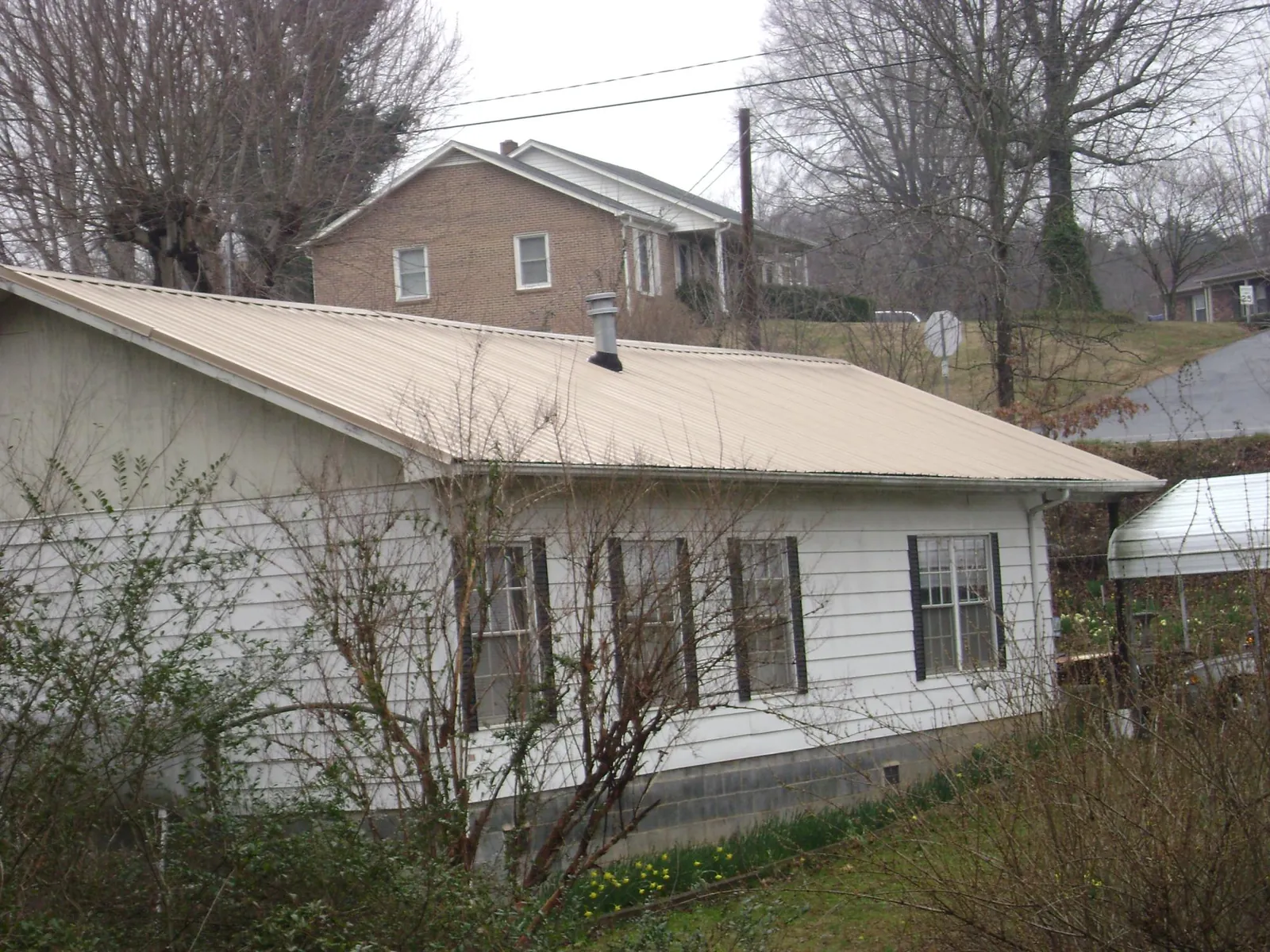 Tan metal roof on a white sided house set into a hillside — Commercial Roofing by Roofing Brothers in Shutesbury