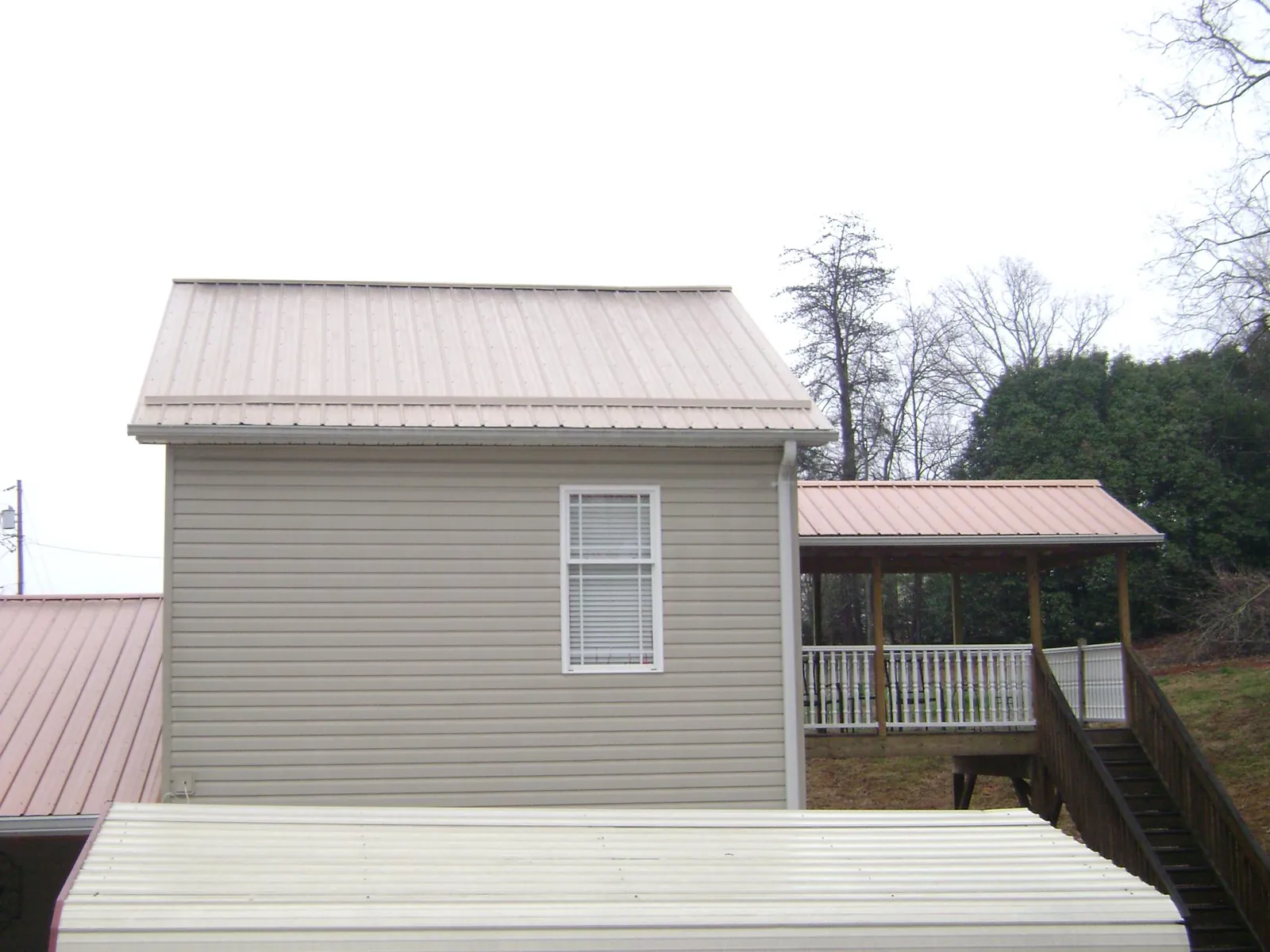 Tan metal roofs on a two story addition and attached porch, from a Roof Replacement job in Shutesbury